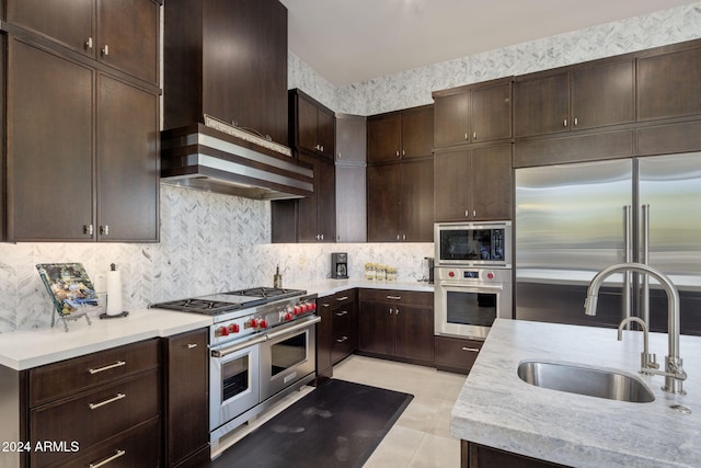 kitchen featuring custom exhaust hood, dark brown cabinets, light tile patterned floors, built in appliances, and sink