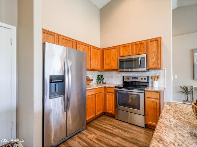 22986 S 208th St, Queen Creek, AZ 85142 - kitchen with stainless steel appliances, high vaulted ceiling, decorative backsplash, dark wood-style flooring, and brown cabinetry