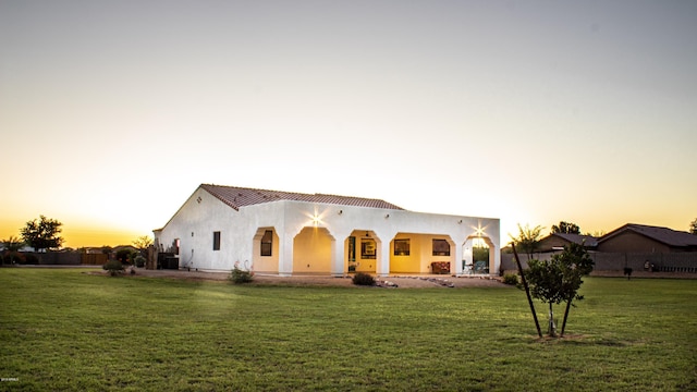 back of house at dusk featuring a yard and stucco siding