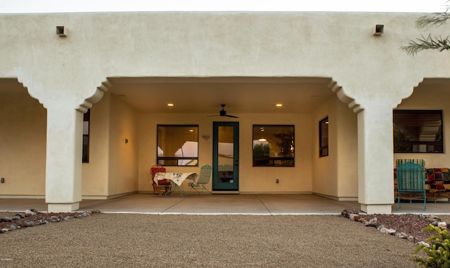 entrance to property featuring a ceiling fan and stucco siding