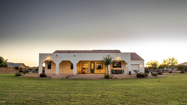 rear view of house featuring an attached garage, a yard, and stucco siding