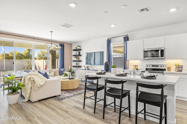 kitchen featuring pendant lighting, appliances with stainless steel finishes, light hardwood / wood-style floors, white cabinets, and a center island with sink