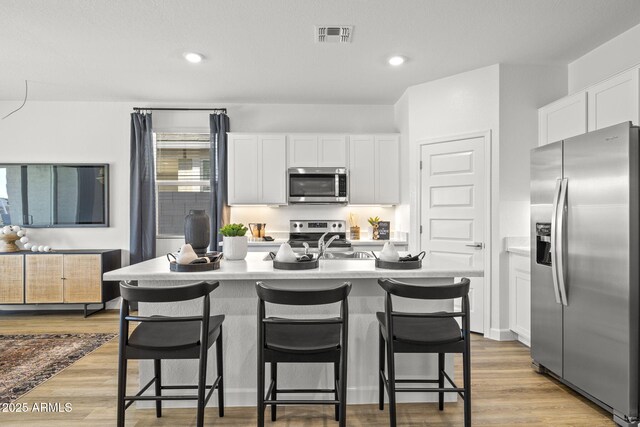 kitchen with white cabinetry, stainless steel appliances, light hardwood / wood-style floors, and a kitchen island with sink