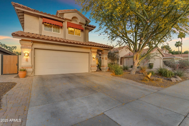 mediterranean / spanish home featuring stucco siding, driveway, a tile roof, and a garage