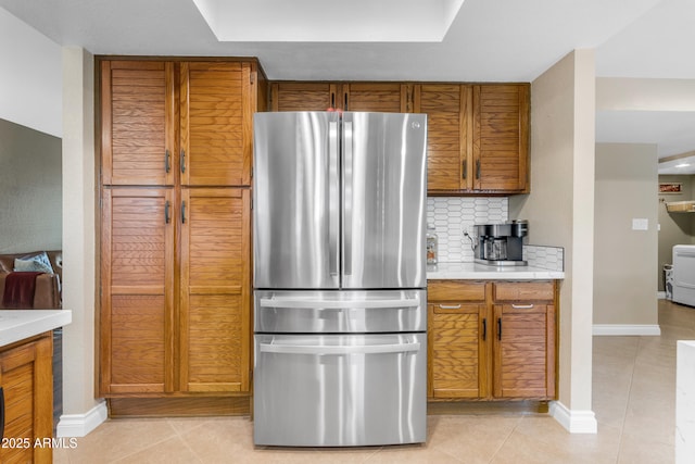 kitchen featuring brown cabinets, light countertops, freestanding refrigerator, light tile patterned floors, and backsplash