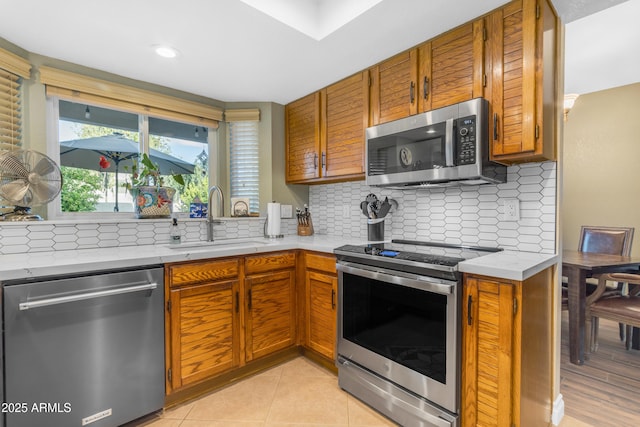 kitchen with a sink, appliances with stainless steel finishes, brown cabinetry, and light countertops