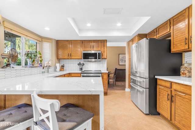 kitchen featuring decorative backsplash, a peninsula, a tray ceiling, a sink, and appliances with stainless steel finishes