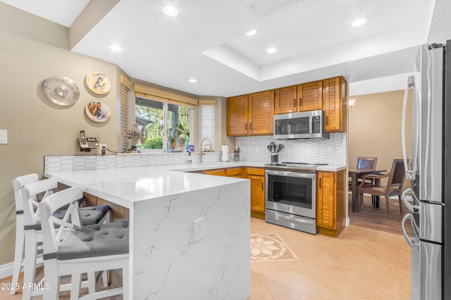 kitchen with visible vents, a peninsula, a breakfast bar area, tasteful backsplash, and stainless steel appliances