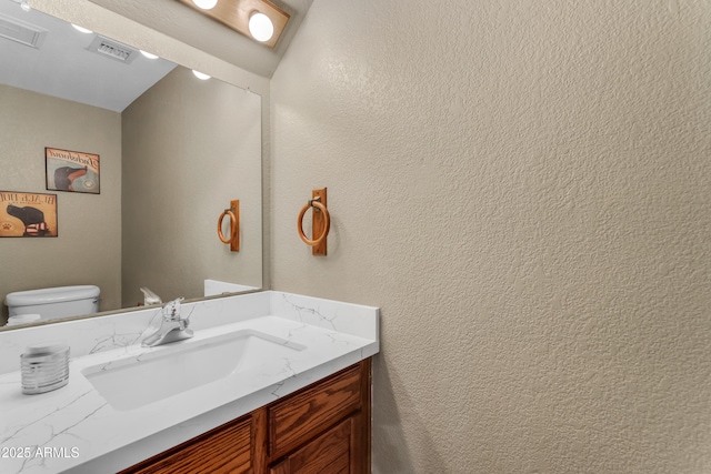 half bath featuring vanity, a textured wall, visible vents, and toilet