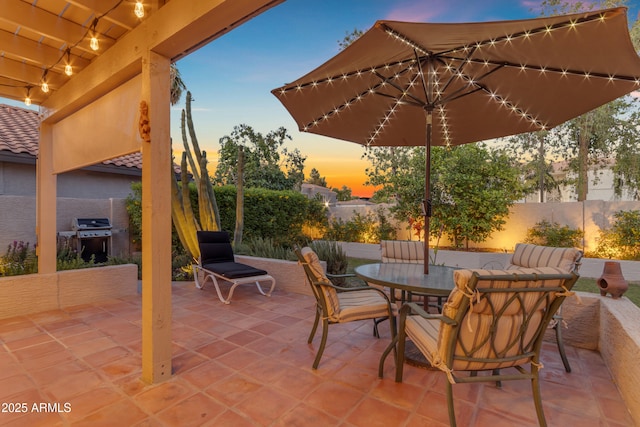 patio terrace at dusk with outdoor dining area, a fenced backyard, and a grill
