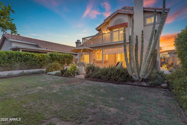 view of front of house with a balcony, stucco siding, a chimney, a tiled roof, and a yard