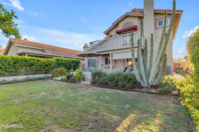 back of property featuring a lawn, stucco siding, a tile roof, and a balcony