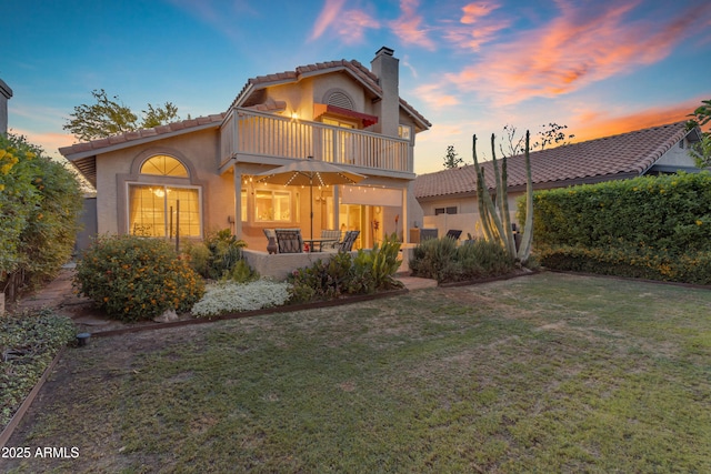 rear view of property featuring a yard, a chimney, a balcony, and stucco siding