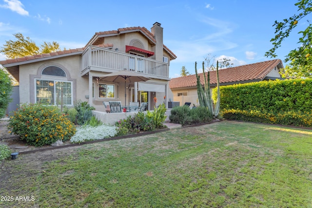 back of property featuring a tiled roof, a chimney, a balcony, a yard, and stucco siding