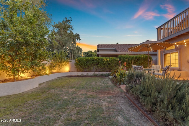 yard at dusk featuring fence and a balcony