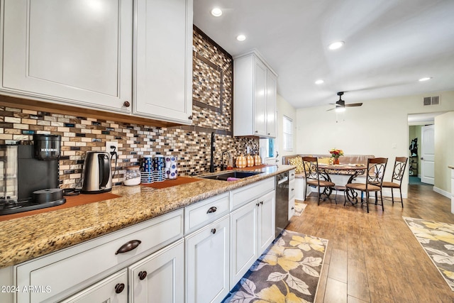 kitchen with decorative backsplash, white cabinetry, light stone countertops, stainless steel dishwasher, and light wood-type flooring