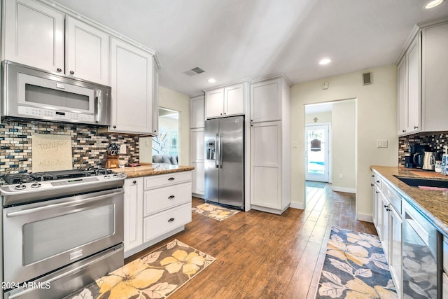 kitchen with tasteful backsplash, appliances with stainless steel finishes, white cabinetry, light hardwood / wood-style floors, and light stone counters