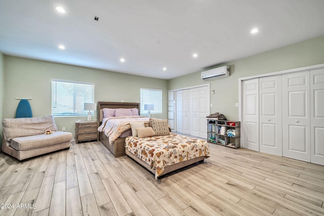 bedroom featuring light hardwood / wood-style flooring, a wall mounted air conditioner, and two closets