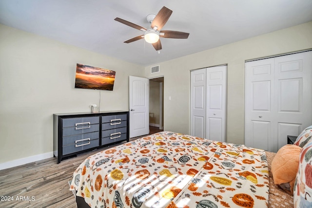 bedroom with multiple closets, hardwood / wood-style flooring, and ceiling fan