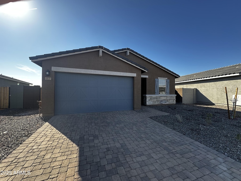 view of front of house featuring a garage, decorative driveway, fence, and stucco siding