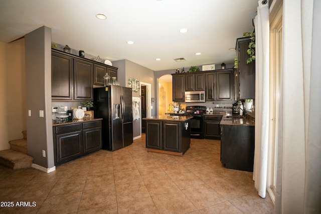 kitchen with a center island, arched walkways, stainless steel appliances, dark countertops, and dark brown cabinetry