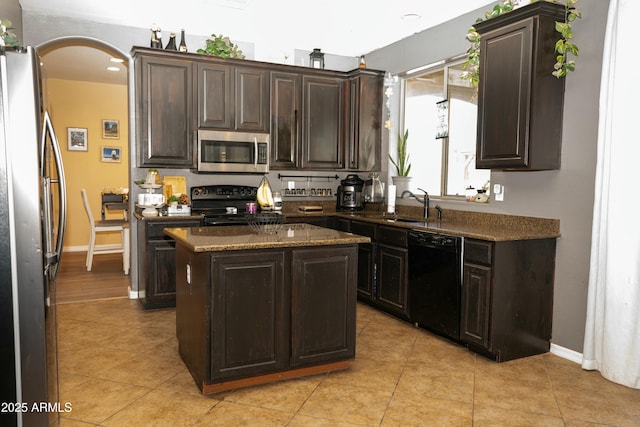 kitchen with dark brown cabinetry, arched walkways, a kitchen island, black appliances, and a sink