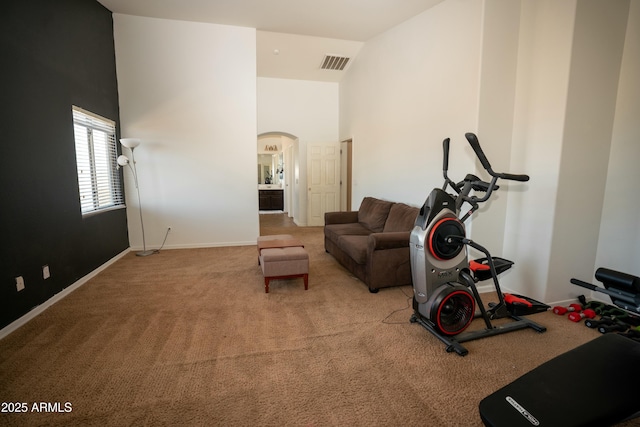 exercise area with arched walkways, light colored carpet, a towering ceiling, baseboards, and visible vents