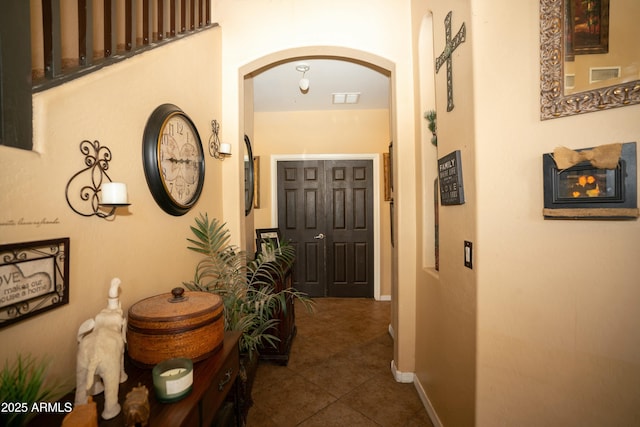 corridor featuring arched walkways, dark tile patterned flooring, visible vents, and baseboards