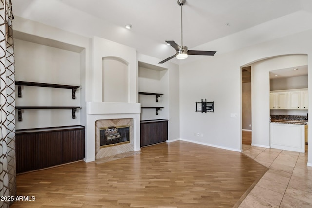 12183 E Mercer Ln, Scottsdale, AZ 85259 - unfurnished living room with a ceiling fan, light wood finished floors, arched walkways, a fireplace, and baseboards