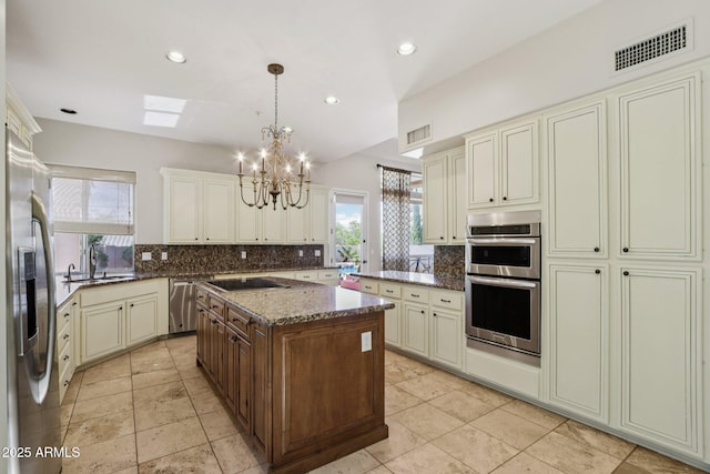 12183 E Mercer Ln, Scottsdale, AZ 85259 - kitchen featuring stainless steel appliances, a sink, a chandelier, cream cabinetry, and tasteful backsplash