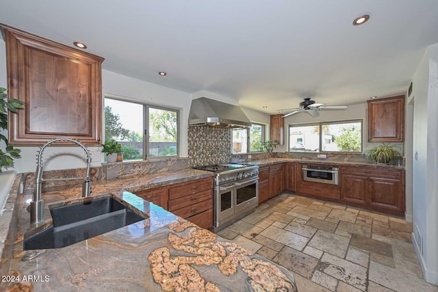 kitchen with sink, wall chimney exhaust hood, ceiling fan, appliances with stainless steel finishes, and stone countertops