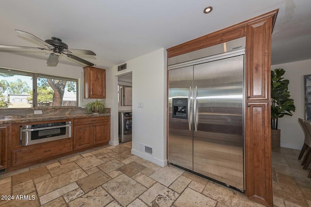 kitchen featuring ceiling fan, washer / clothes dryer, appliances with stainless steel finishes, and dark stone counters