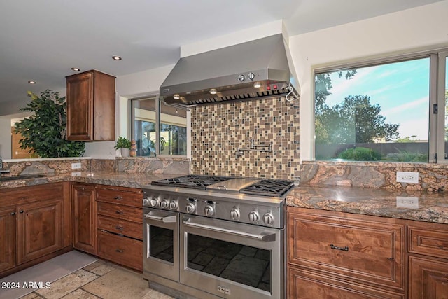 kitchen with dark stone countertops, sink, wall chimney exhaust hood, and range with two ovens