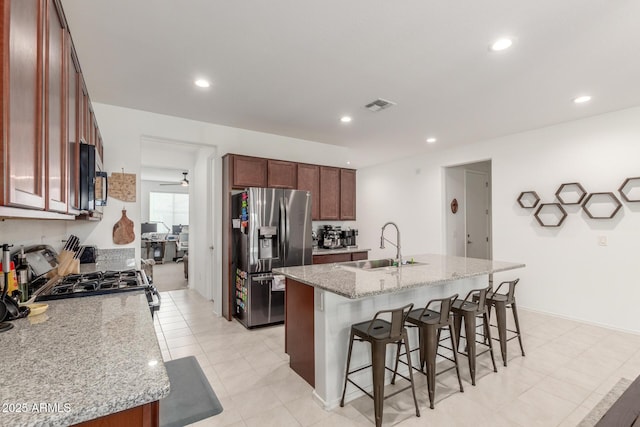 kitchen featuring sink, light stone counters, stainless steel fridge, an island with sink, and range