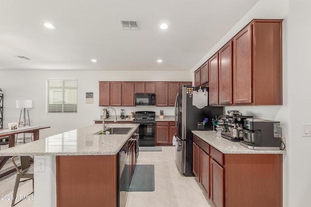 kitchen featuring light stone countertops, sink, black appliances, a center island with sink, and a breakfast bar area