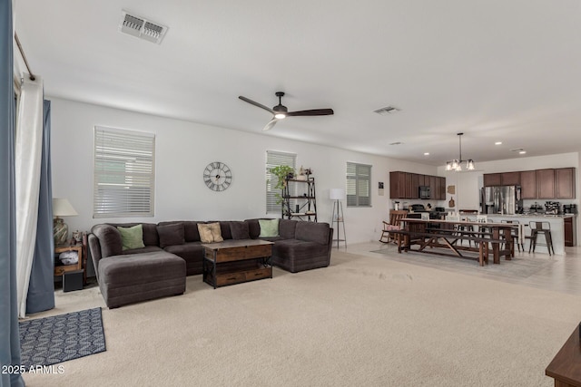 carpeted living room featuring ceiling fan with notable chandelier