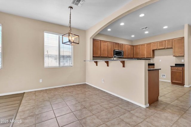 209 E Diamond Trl, San Tan Valley, AZ 85143 - kitchen with stainless steel microwave, brown cabinets, a kitchen bar, a peninsula, and dark countertops