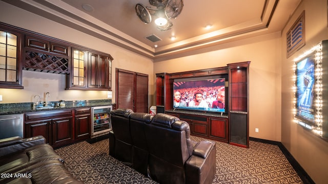 carpeted cinema room with beverage cooler, wet bar, and a raised ceiling