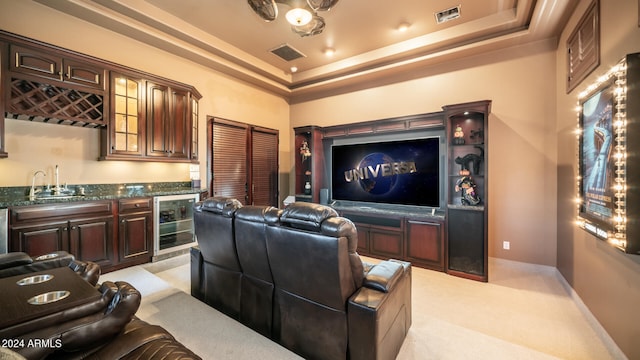 home theater room with light colored carpet, beverage cooler, indoor wet bar, and a raised ceiling