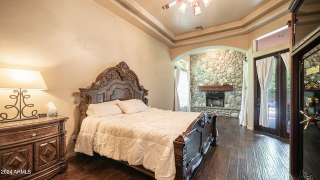 bedroom featuring ceiling fan, a raised ceiling, dark wood-type flooring, a fireplace, and access to exterior