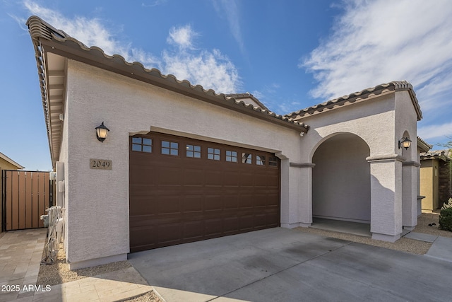 mediterranean / spanish house with a garage, concrete driveway, a tiled roof, fence, and stucco siding