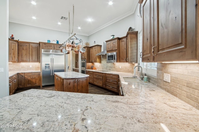 kitchen with light stone counters, ornamental molding, sink, built in appliances, and a kitchen island