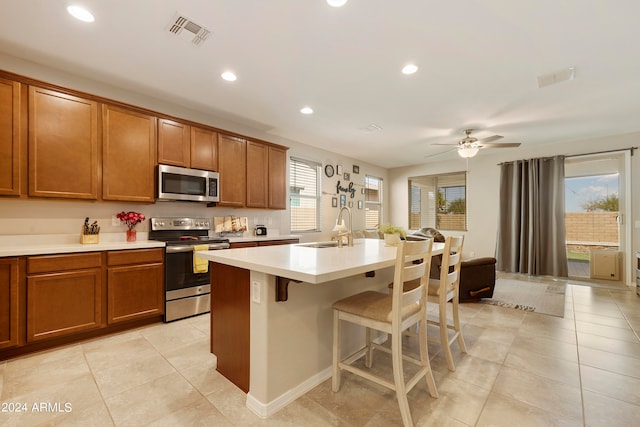 kitchen with a kitchen bar, stainless steel appliances, a center island, sink, and ceiling fan