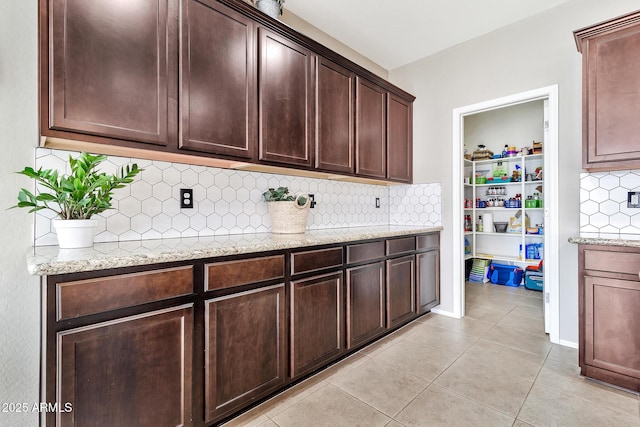 kitchen with light stone counters, tasteful backsplash, dark brown cabinetry, and light tile patterned floors