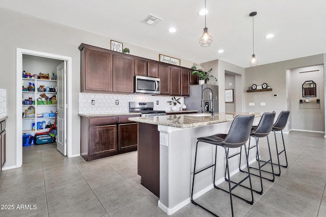 kitchen with visible vents, a center island with sink, backsplash, stainless steel appliances, and dark brown cabinets