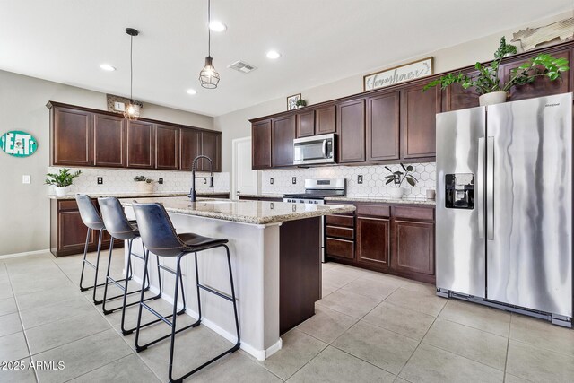 kitchen with light stone countertops, visible vents, light tile patterned flooring, appliances with stainless steel finishes, and backsplash