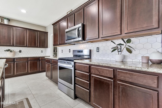 kitchen featuring light tile patterned floors, light stone countertops, stainless steel appliances, decorative backsplash, and dark brown cabinetry