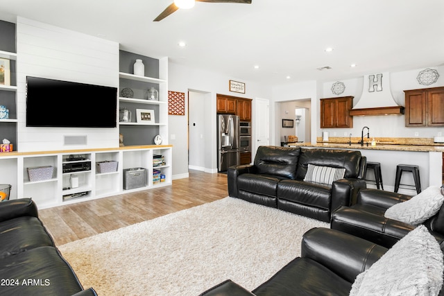 living room with ceiling fan, sink, and light wood-type flooring