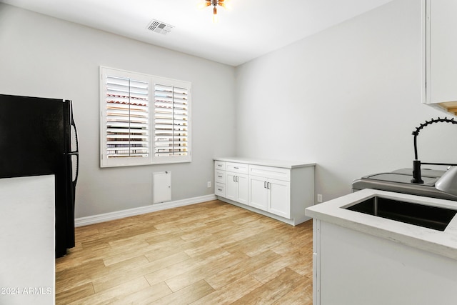 kitchen with light wood-type flooring, sink, black fridge, and white cabinetry