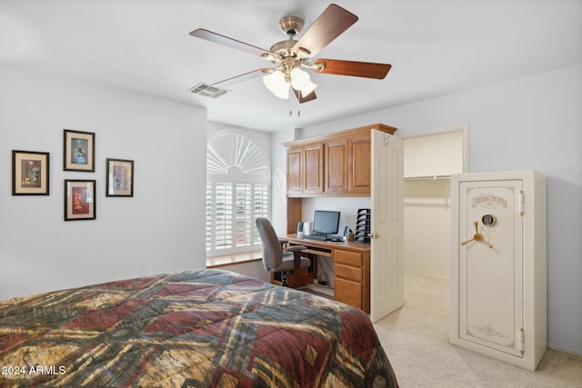 carpeted bedroom with built in desk, ceiling fan, and a walk in closet